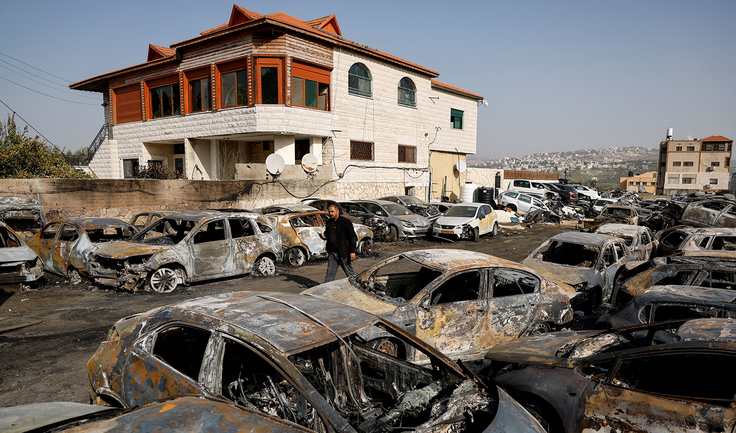 A man walks among cars burnt in an attack by Israeli settlers near Hawara in the Israeli-occupied West Bank, February 27, 2023. (REUTERS)