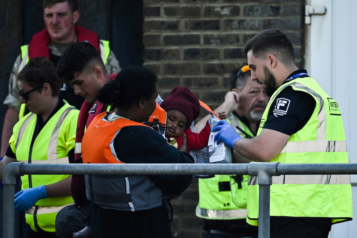 A woman holds a baby who has his life jacket removed by an Interforce officer, after they disembark from the UK Border Force vessel BF Hurricane. (File/AFP)