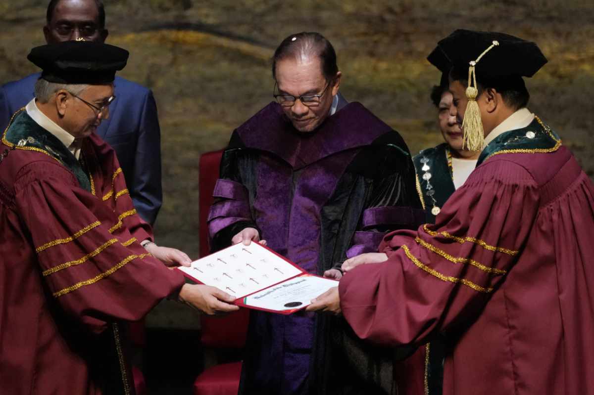 Malaysia's Prime Minister Anwar Ibrahim, center, is conferred a Doctor of Laws degree, honoris causa, led by Angelo Jimenez, right, president of the University of the Philippines on March 2, 2023. (AP Photo/Aaron Favila)