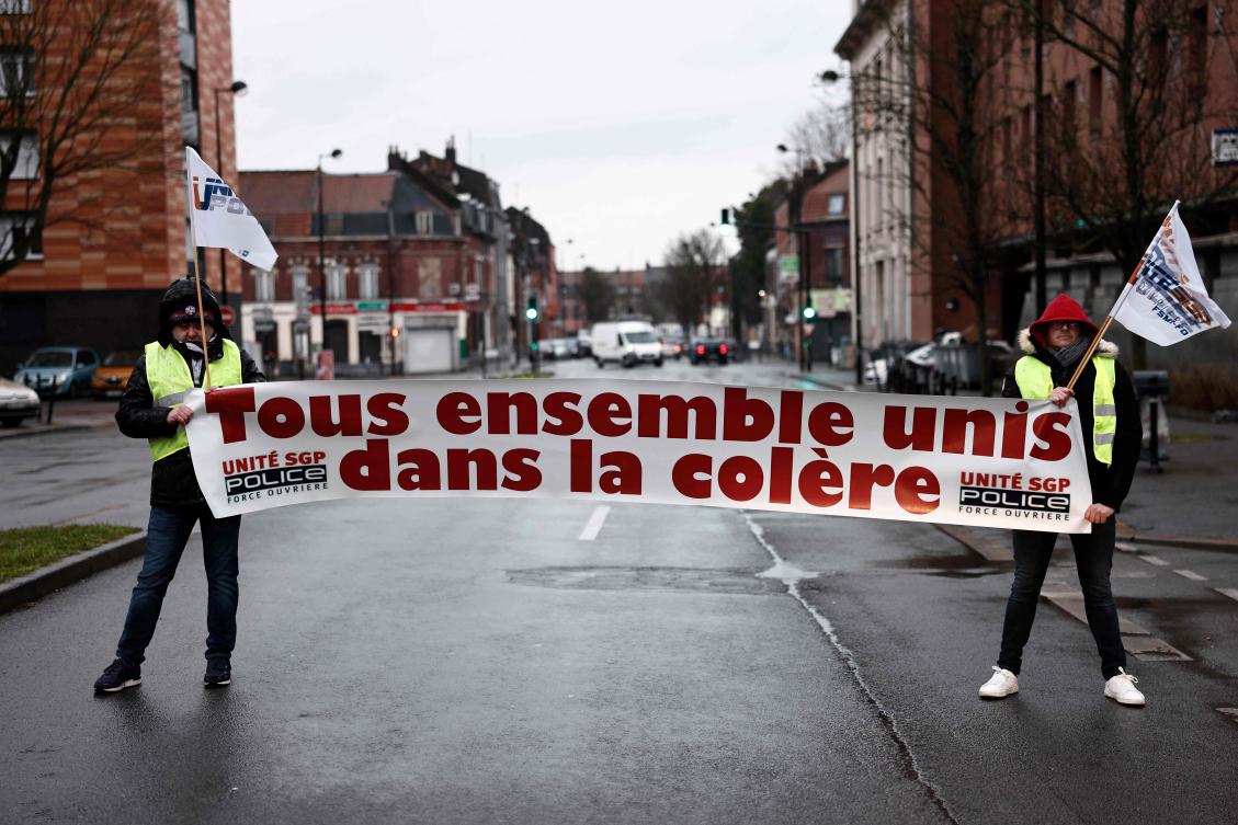Police hold a banner that reads, ' All together untited in anger' as they protest nationwide against French President's pension reform and its postponement of the legal retirement age from 62 to 64. (AFP)