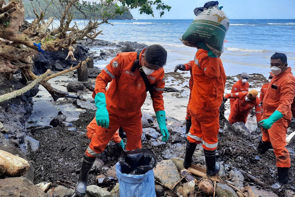 Philippine coast guard personnel and volunteers collect debris covered with oil during a clean-up at Pola, Oriental Mindoro, Mar. 8, 2023, days after an oil spill from a sunken tanker. (AFP)
