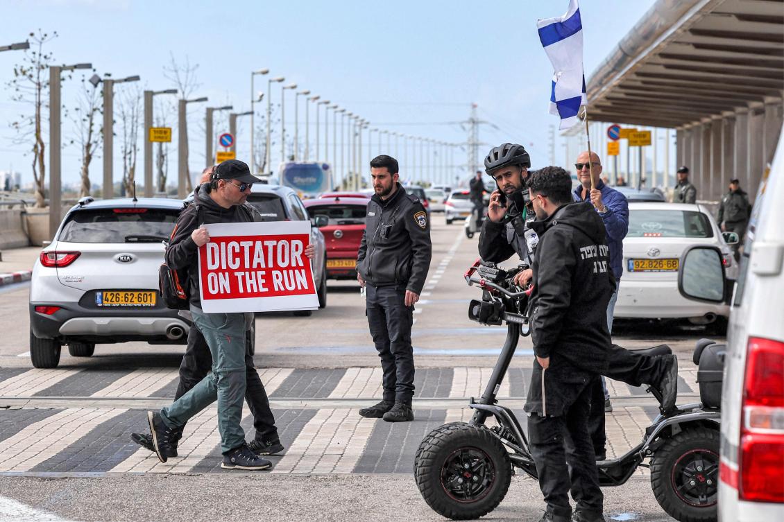 A demonstrator walks with a sign reading in English “dictator on the run,” referring to PM Benjamin Netanyahu who heads to Germany on an official visit, during a protest against the controversial judicial reform bill outside the terminal of Israel’s Ben Gurion airport on Wednesday. (AFP)