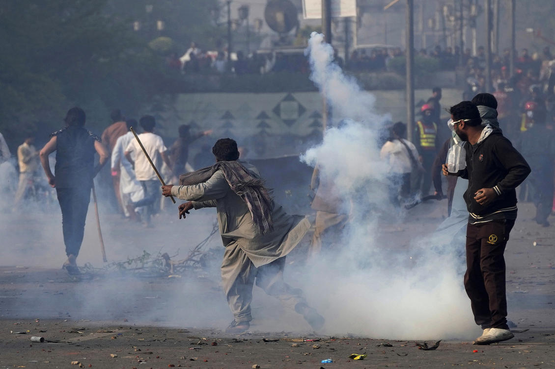 A supporter of former Prime Minister Imran Khan hurls back a tear gas shell fired by riot police officers to disperse them during clashes, in Lahore on March 15, 2023. (AP)