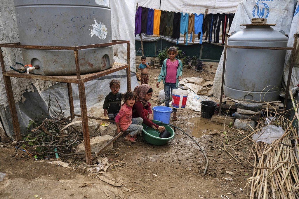 Children sit by as a woman washes dishes in a plastic basin outside a tent at a make-shift camp for Syrian refugees in Talhayat in the Akkar district in north Lebanon. (AFP)