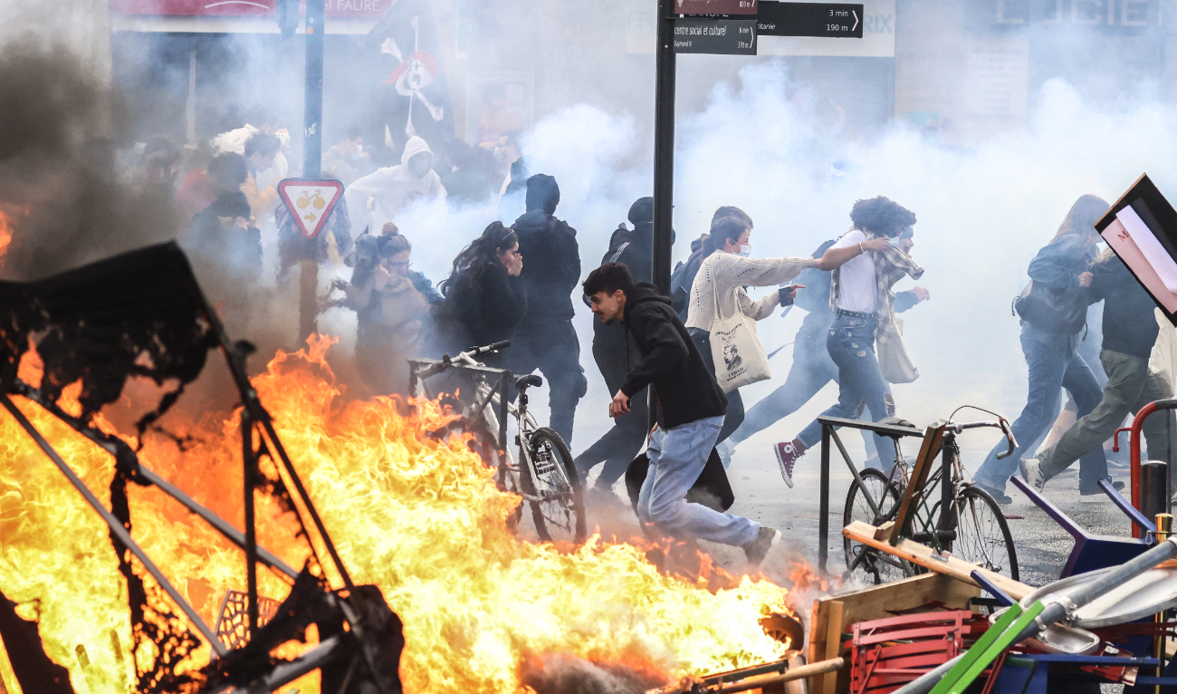 Protesters run in tear gas smoke next to a street fire on the sidelines of a demonstration as part of a national day of strikes and protests in Toulouse, southern France, on March 23, 2023. (AFP)