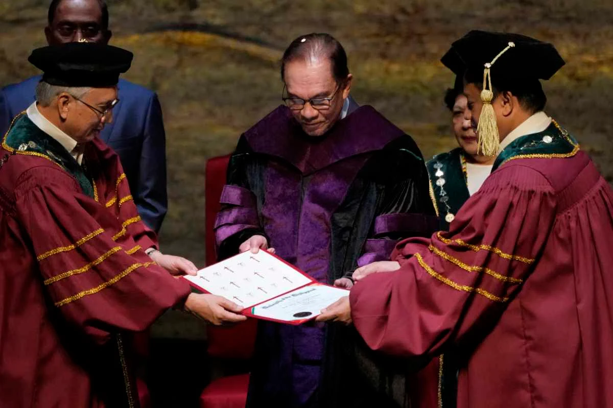 Malaysia's Prime Minister Anwar Ibrahim, center, is conferred a Doctor of Laws degree, honoris causa, led by Angelo Jimenez, right, president of the University of the Philippines on March 2, 2023. (AP Photo/Aaron Favila)