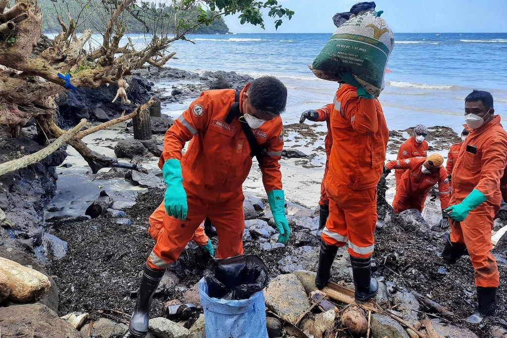 Philippine coast guard personnel and volunteers collect debris covered with oil during a clean-up at Pola, Oriental Mindoro, Mar. 8, 2023, days after an oil spill from a sunken tanker. (AFP)