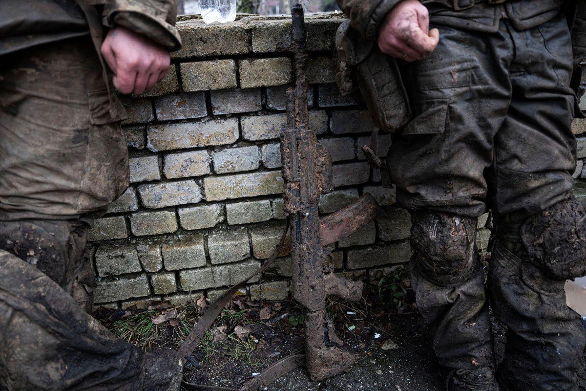 A mud-stained gun is seen in front of Ukrainian servicemen who just come back from the trenches of Bakhmut in Chasiv Yar, Ukraine, on March 8, 2023. (AP)