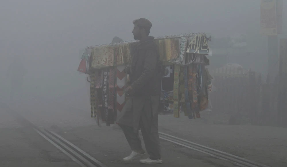 A vendor crosses a rail track amid smoggy and foggy conditions early in the morning in Lahore on January 3, 2023. (AFP)