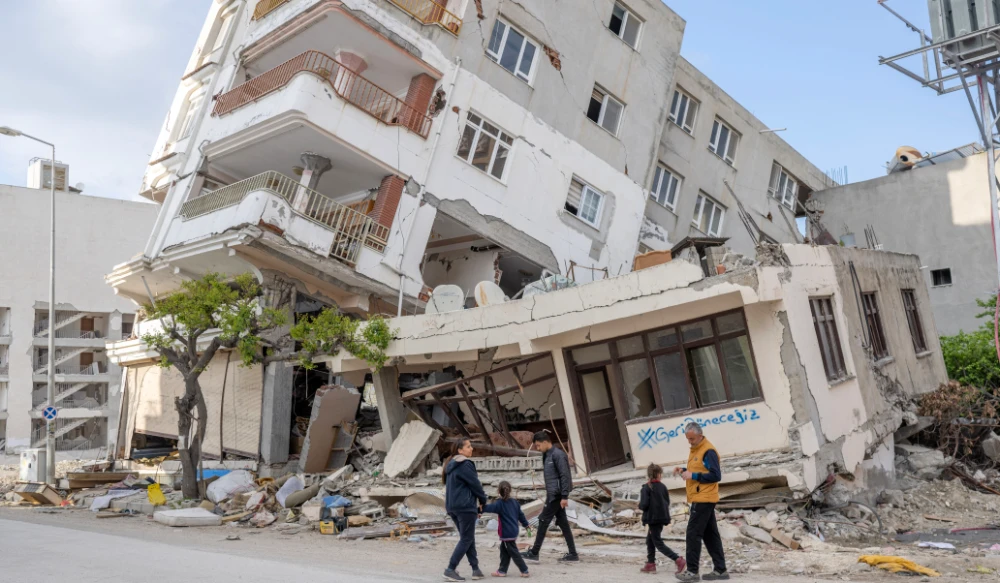 Kenan Civi and his family gather in front of their damaged house bearing a graffiti inscription which reads "we will come back", in Hatay on March 28, 2023, after a 7.8-magnitude earthquake struck on February 6, 2023 in southeastern Turkey. (AFP)
