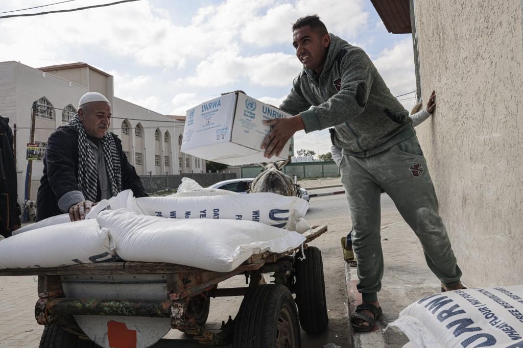 Palestinians carry bags of flour and other food products received as aid to poor families, at the UNRWA distribution center in the Rafah refugee camp, Gaza Strip. (File/AFP)