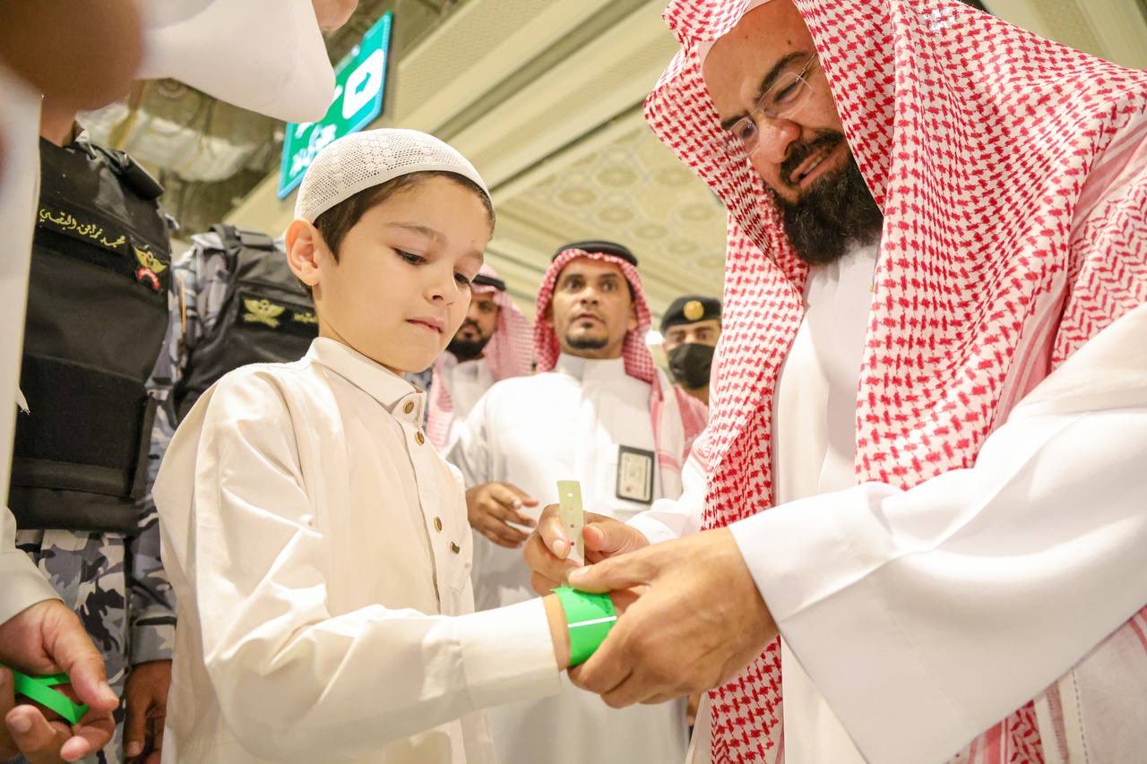 Sheikh Abdulrahman Al-Sudais helps a child put his identification wristband on at the Grand Mosque in Makkah. (@ReasahAlharmain)