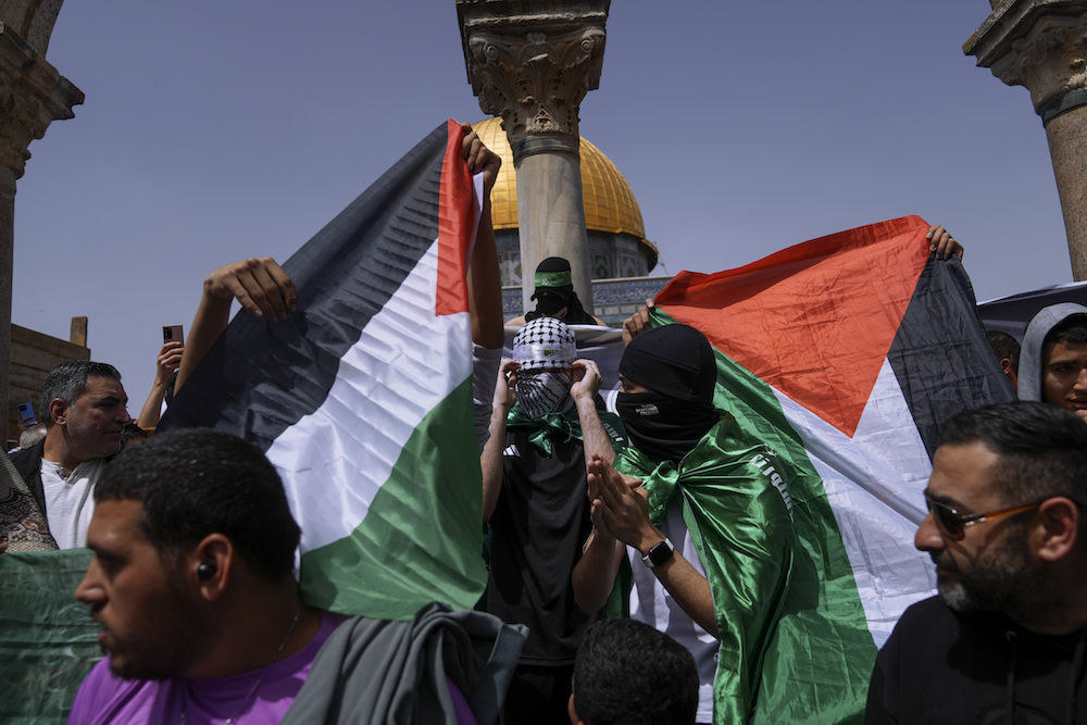 Palestinians hold the Palestinian national flag and the flag of the Hamas militant group during a protest by the Dome of Rock at the Al-Aqsa Mosque compound. (AP)
