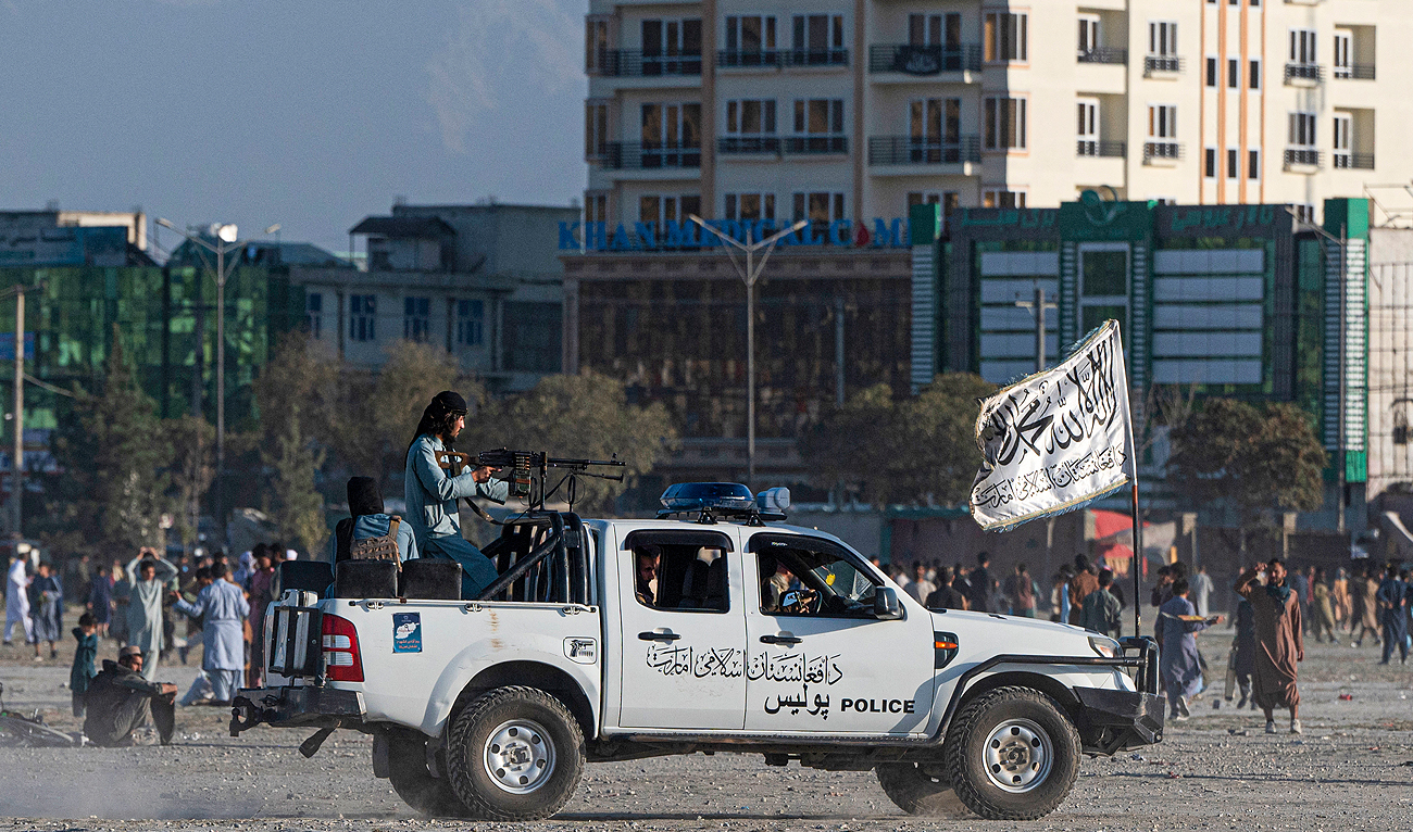 In this picture taken on October 21, 2022, Taliban fighters ride a vehicle as Afghan men play cricket at the Chaman-e-Huzuri ground in Kabul. (Photo courtesy: AFP)