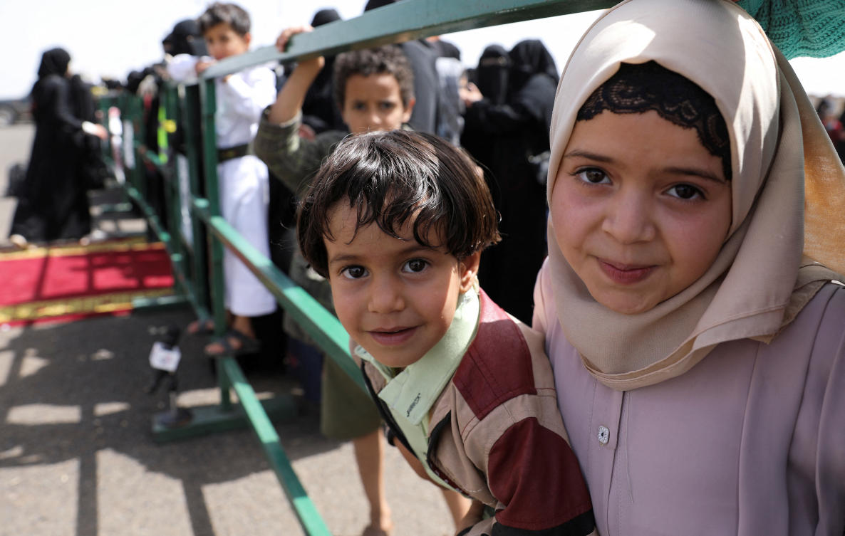 Children stand behind a barrier as relatives of freed prisoners wait for an ICRC-chartered plane carrying freed prisoners to land at Sanaa Airport, amid a prisoner swap between two sides in the Yemen conflict, in Sanaa, Yemen April 16, 2023. (Reuters)
