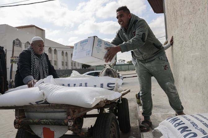 Palestinians carry bags of flour and other food products received as aid to poor families, at the UNRWA distribution center in the Rafah refugee camp, Gaza Strip. (AFP/File)