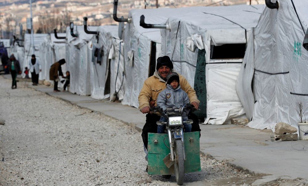 A displaced Syrian man and his son ride a motorcycle, as they drive between the tents at a refugee camp, in Bar Elias, in eastern Lebanon’s Bekaa Valley, March 5, 2021. (AP Photo)