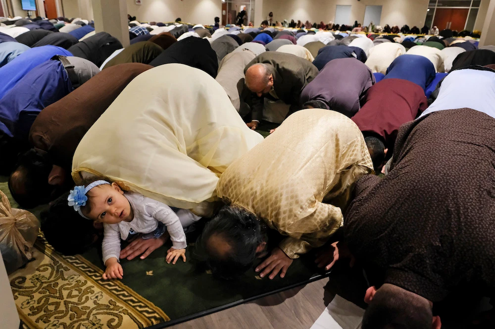 Samar Mansour, peeks out from the arms of her father, Ahmed Mansour, as he prays during the Islamic Society of North West Ohio Eid celebration. (AP)