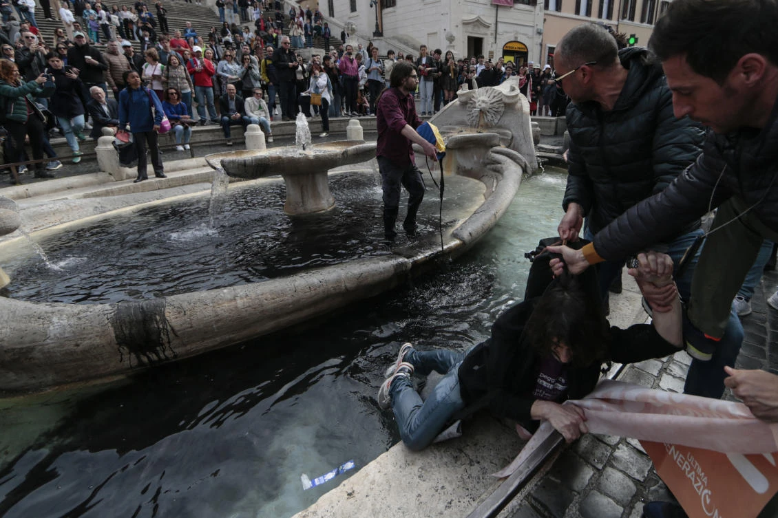 An environmental activist is removed from the “Fontana della Barcaccia” (Fountain of the Boat) by police as the other activist pours black paint inside the fountain during a protest action at the Piazza di Spagna in Rome on Apr. 1, 2023. (AP)