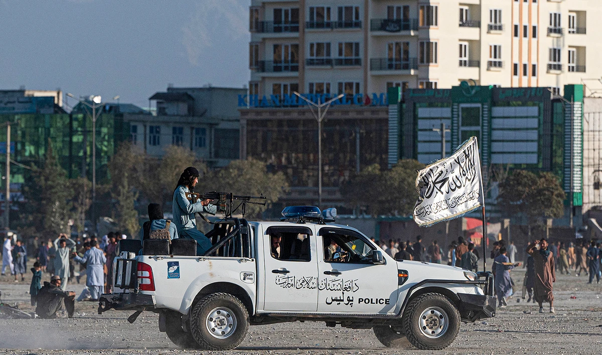 In this picture taken on October 21, 2022, Taliban fighters ride a vehicle as Afghan men play cricket at the Chaman-e-Huzuri ground in Kabul. (Photo courtesy: AFP)