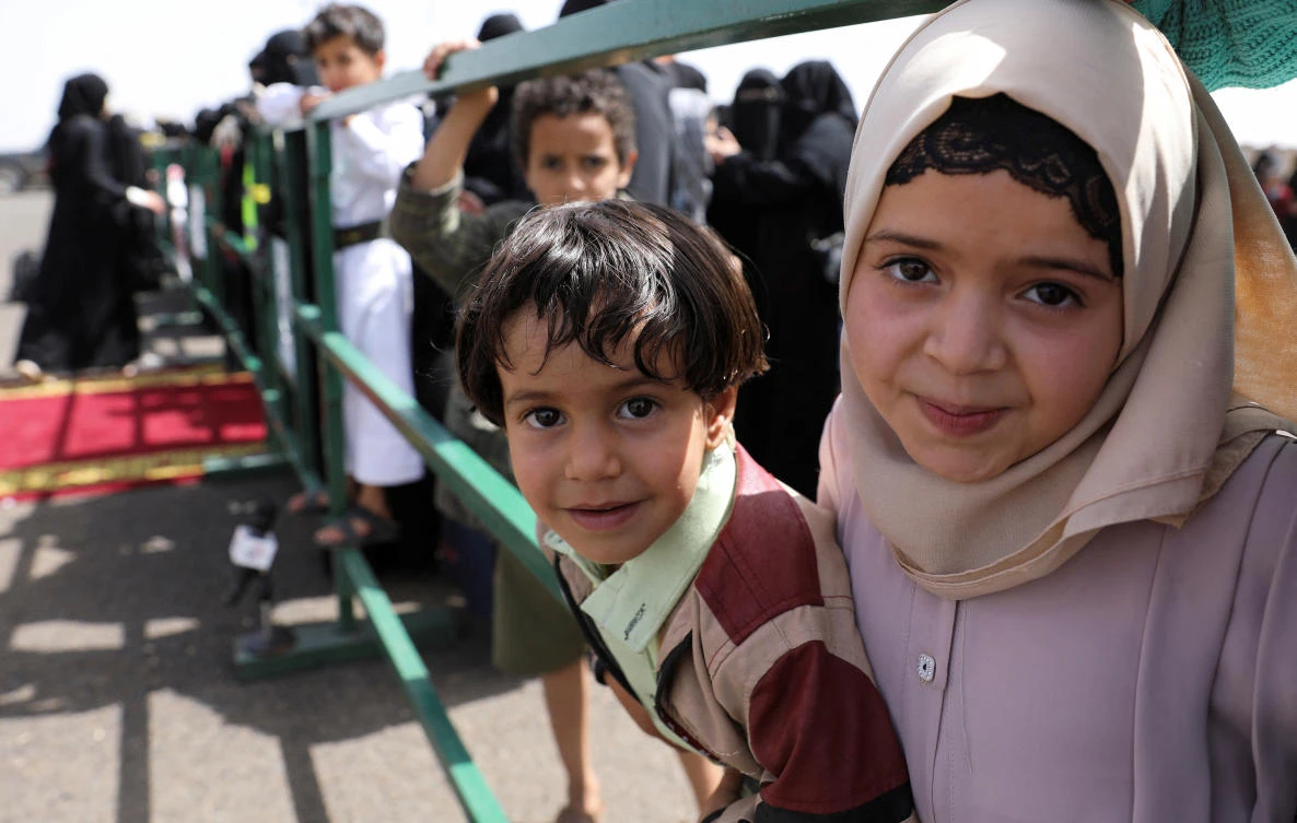 Children stand behind a barrier as relatives of freed prisoners wait for an ICRC-chartered plane carrying freed prisoners to land at Sanaa Airport, amid a prisoner swap between two sides in the Yemen conflict, in Sanaa, Yemen April 16, 2023. (Reuters)