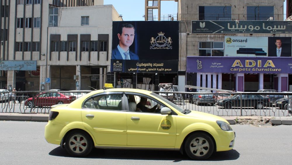 A car passes by a poster of Syrian President Bashar Assad in Damascus, Syria, May 16, 2023. (Reuters)