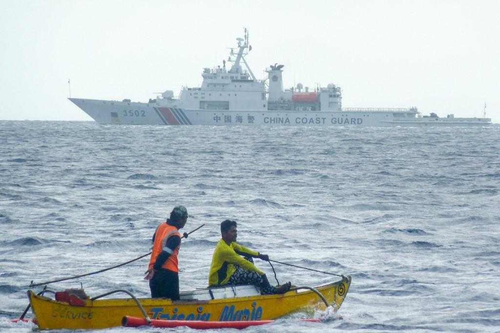 China claims sovereignty over almost the entire South China Sea. Above, Filipino fishermen aboard their wooden boat sail past a Chinese coast guard ship in Scarborough Shoal in the South China Sea on Dec. 23, 2022. (AFP)
