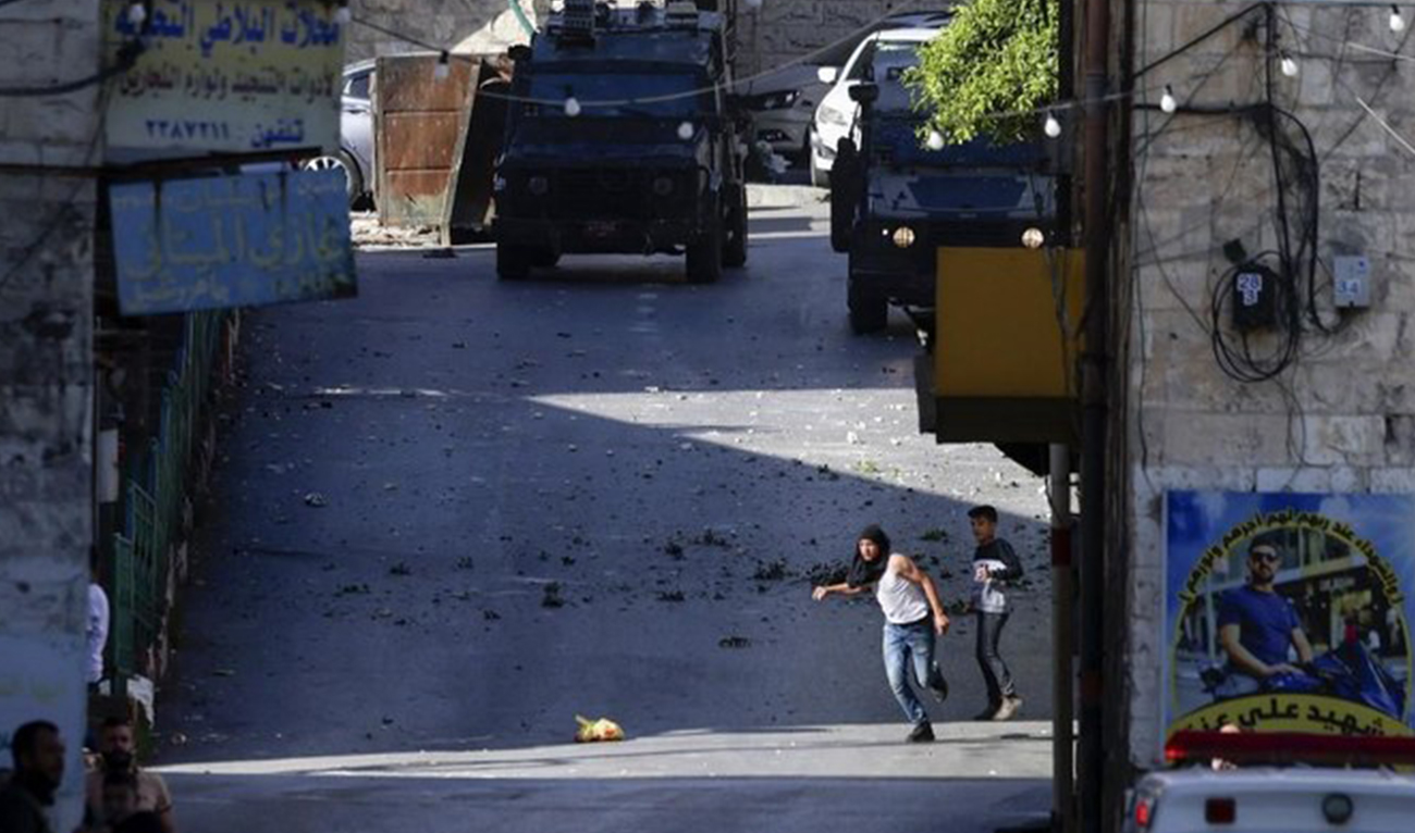 Palestinians take cover as they clash with Israeli forces during an Israeli army raid in the occupied West Bank city of Nablus on May 4, 2023. (AFP)