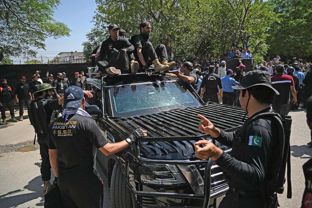 Security personnel escort a car carrying Pakistan’s former Prime Minister Imran Khan as he arrives at the high court in Islamabad on May 9, 2023. (AFP)