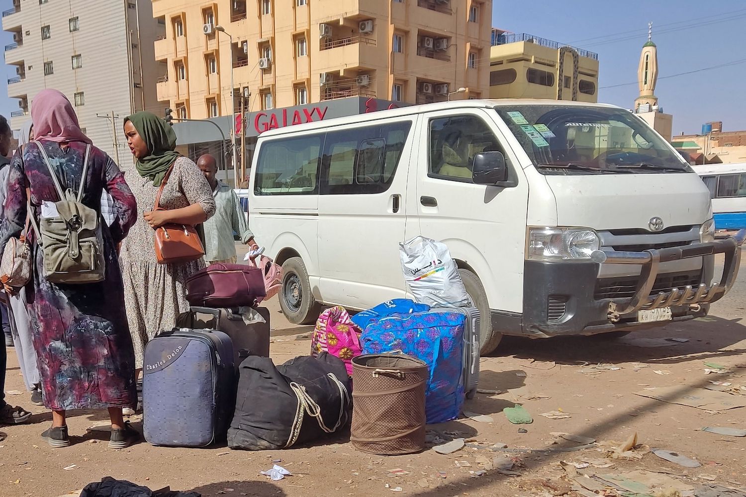 People wait with their luggage at a bus stop in southern Khartoum on May 8, 2023 as fighting continues between Sudan’s army and the paramilitary forces. (AFP)