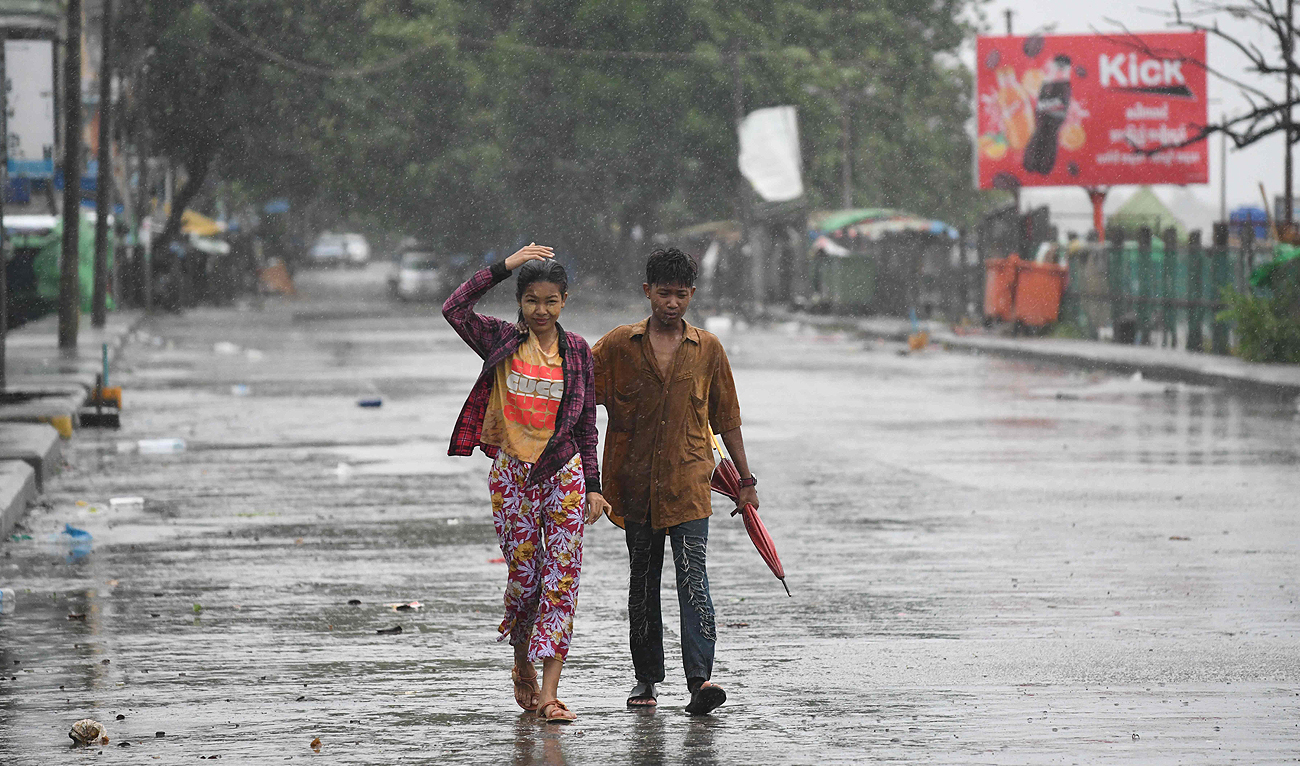 Pedestrians walk in an empty street under the rains after Cyclone Mocha’s crashed ashore, in Kyauktaw in Myanmar’s Rakhine state on May 14, 2023. (Photo courtesy: AFP)