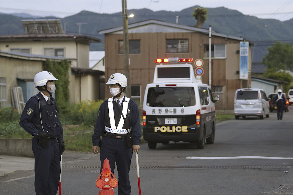 Above, police officers stand guard on a street leading to a building where a man is holed up in Nakano, central Japan on May 25, 2023. (Kyodo News via AP)