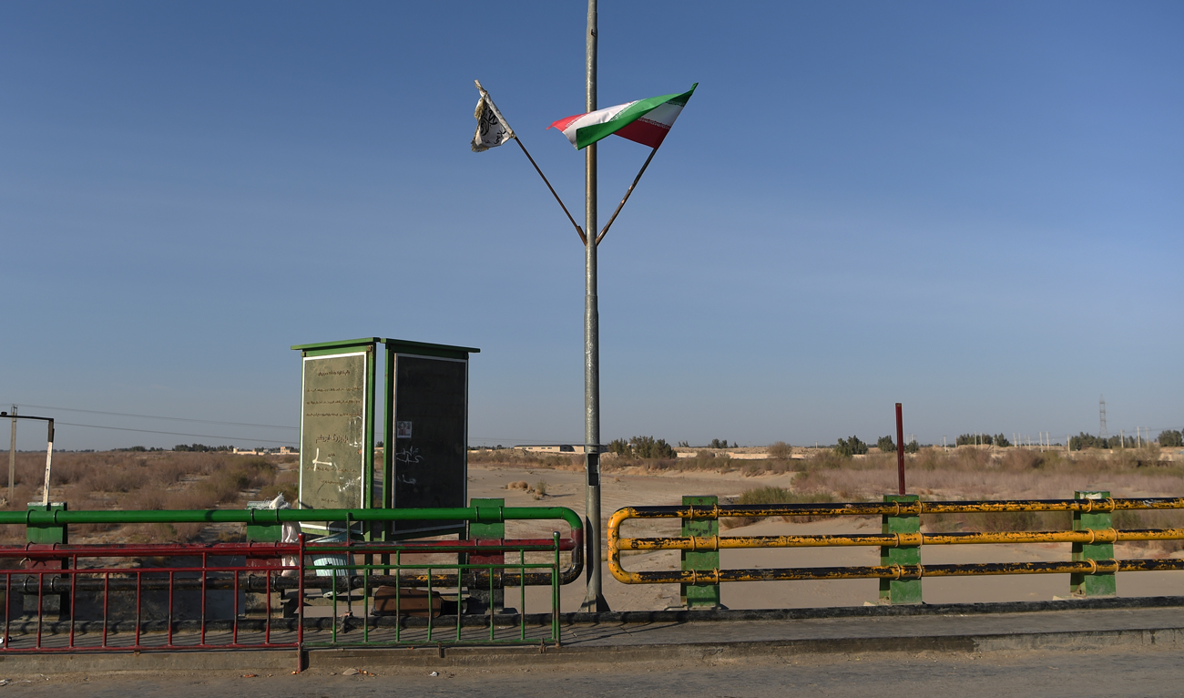 In this photo taken on February 18, 2022 a Taliban flag (L) and an Iranian flag wave at the zero point of Afghan-Iran border crossing bridge in Zaranj. (Photo courtesy: AFP)