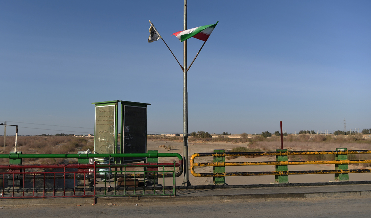 In this photo taken on February 18, 2022 a Taliban flag (L) and an Iranian flag wave at the zero point of Afghan-Iran border crossing bridge in Zaranj. (AFP/File)