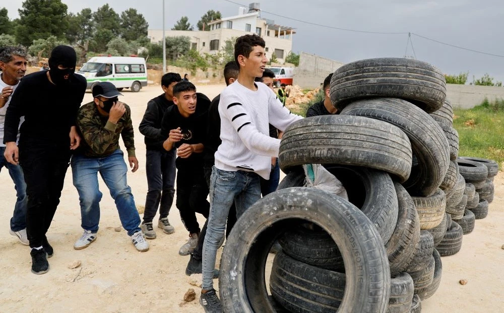 Palestinian demonstrators take cover behind tires during a protest against Israeli settlements near Nablus in the Israeli-occupied West Bank, April 10, 2023. (Reuters)