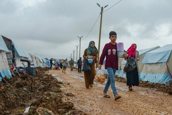 People carry food on a muddy path next to tents donated by Turkish Turk Kizilay humanitarian organization. (File/AFP)
