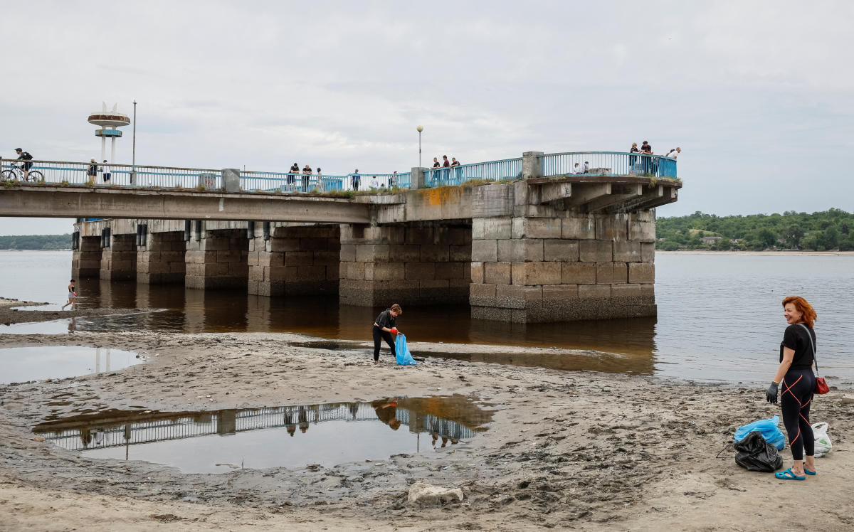 Local residents clean a city beach, which became full of rubbish after a water level in Dnipro river sharply dropped, following Kakhovka dam destruction, amid Russia's attack on Ukraine, in Zaporizhzhia, Ukraine, June 10, 2023. (Reuters)