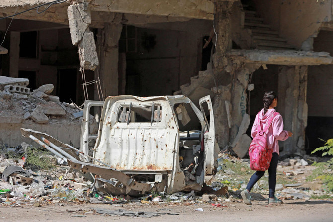 A young girl walks past a damaged vehicle and destroyed building in the southern suburbs of Damascus on Nov. 2, 2022. (AFP/File)
