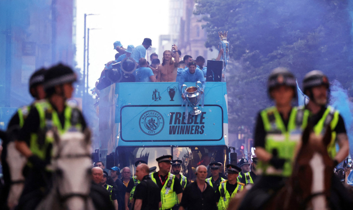 Manchester City's John Stones is pictured holding the Champions League trophy alongside Erling Haaland and teammates as mounted police officers escort the parade through Manchester. (Reuters)