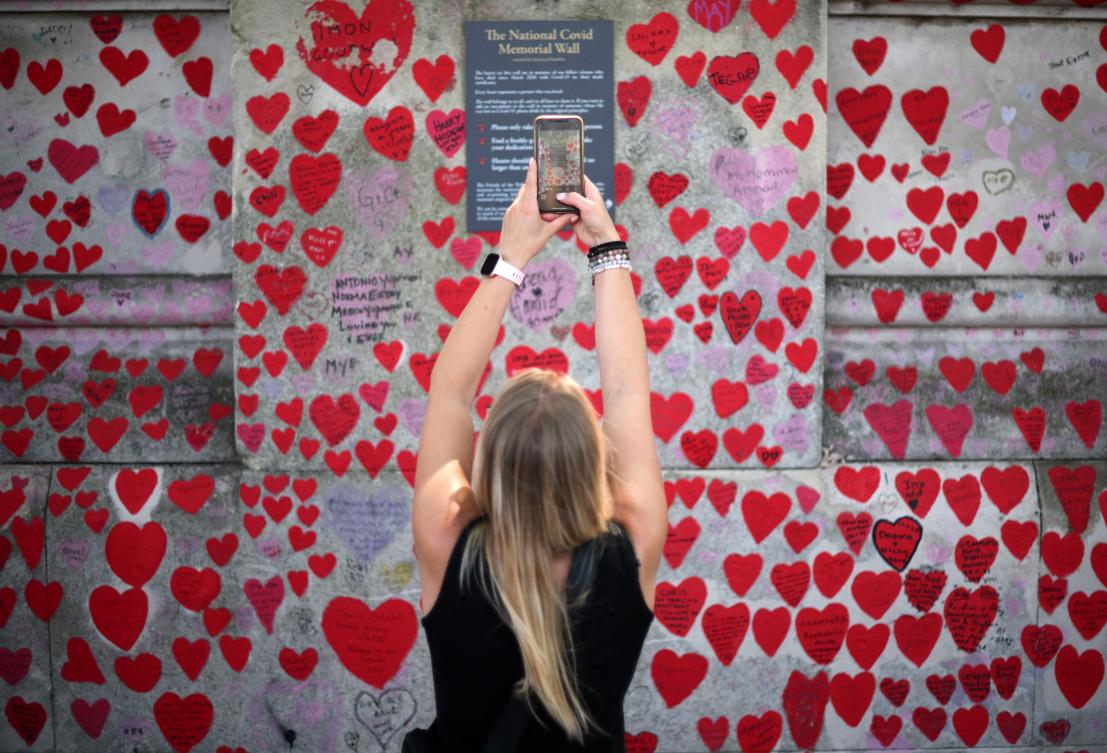 A person takes a photograph of the plaque on the National Covid Memorial Wall, dedicated to those who lost their lives to Covid-19, on the embankment on the south side of the River Thames in London on June 13, 2023. (AFP)