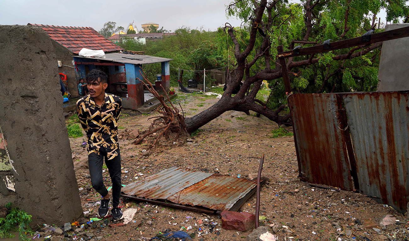 A man walks past a fallen tree at his house in the coastal town of Mandvi as cyclone Biparjoy makes landfall on June 16, 2023. (AFP)
