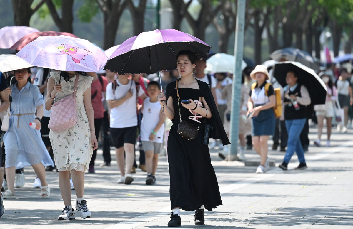 People shelter from the sun under umbrellas after visiting the Forbidden City during a heatwave in Beijing on Saturday. (AFP)