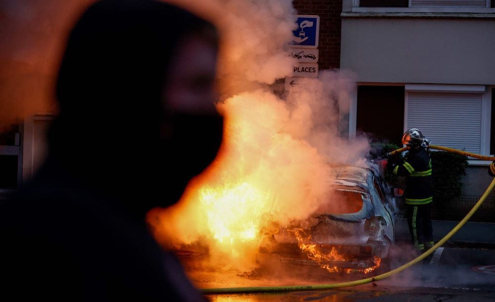 A firefighter puts out a burning car during protests in Lille, northern France, on June 29, 2023, two days after a teenager was shot dead during a police traffic stop in the Paris suburb of Nanterre. (AFP)