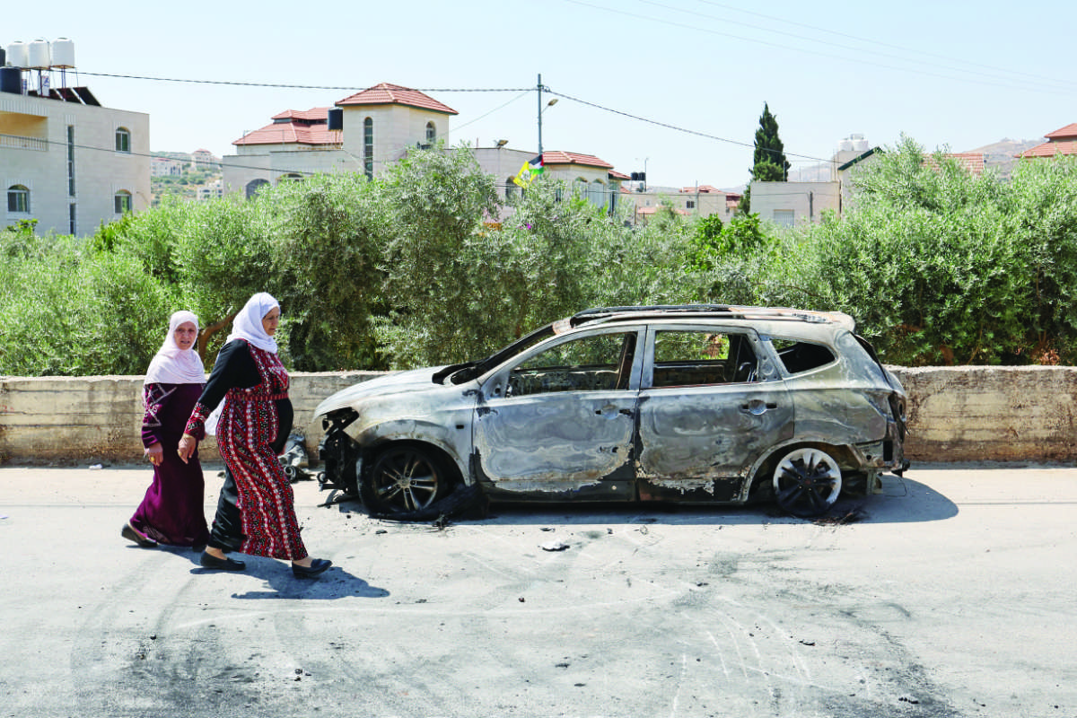 Palestinians walk past a burnt car, which was set on fire by Israeli settlers, near the occupied West Bank city of Ramallah. (AFP file photo)