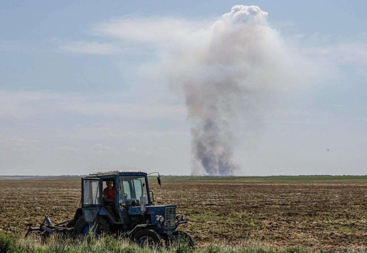 An agricultural worker operates a tractor as smoke rises in the distance after a military strike, amid Russia's attack on Ukraine, in Kherson region, Ukraine June 20, 2023. (REUTERS)