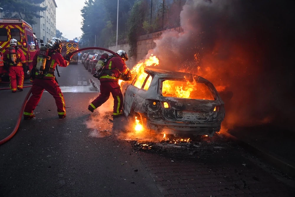 Firefighters work to put out a burning car on the sidelines of a demonstration in Nanterre, west of Paris. (AFP)