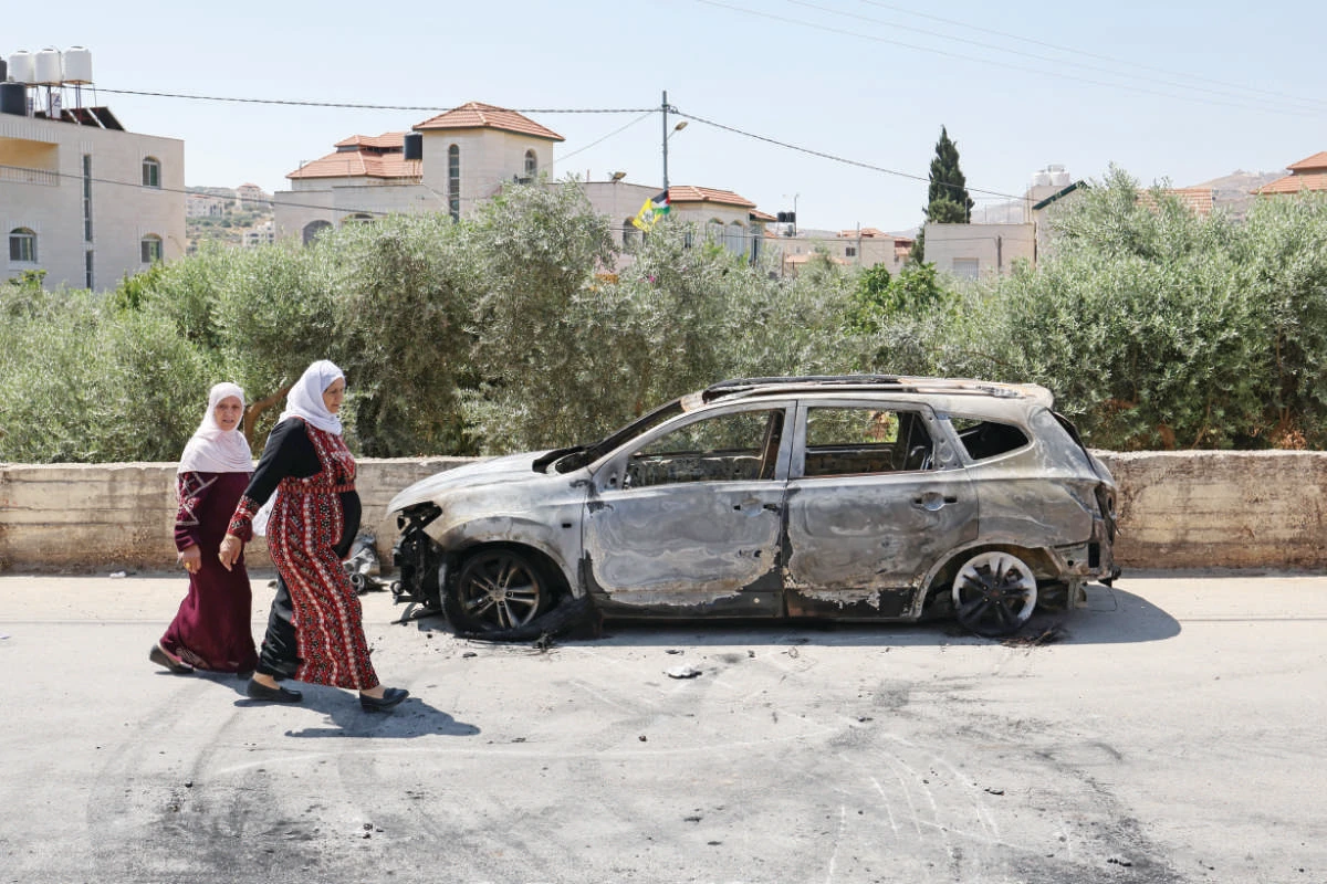 Palestinians walk past a burnt car, which was set on fire by Israeli settlers, near the occupied West Bank city of Ramallah. (AFP file photo)