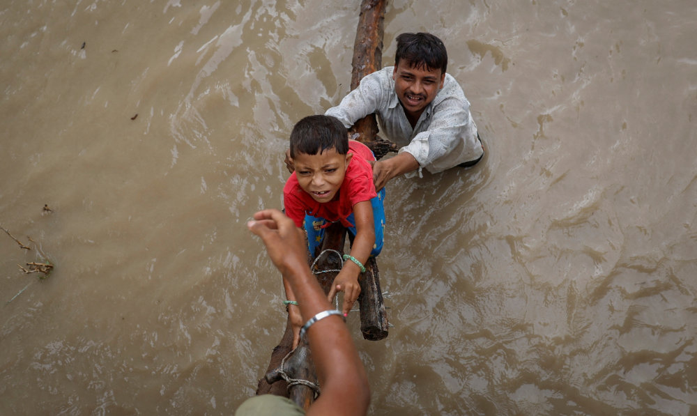 A man helps his son to climb onto a flyover under construction, after being displaced by the rising water level of river Yamuna after heavy monsoon rains in New Delhi, India, July 12, 2023. (Reuters)