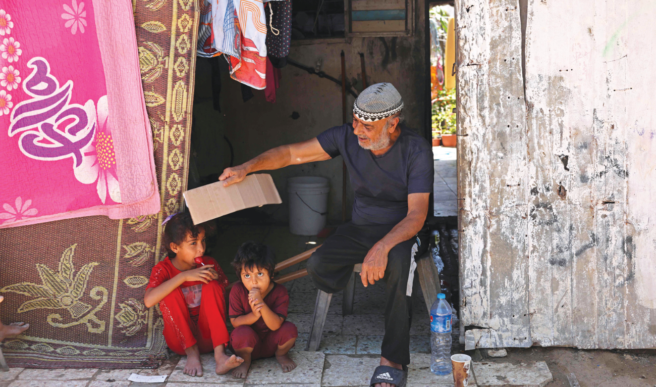 A Palestinian father uses a piece of cardboard to keep his children cool amidst soaring temperatures and power cuts in Gaza on Tuesday. (AFP)