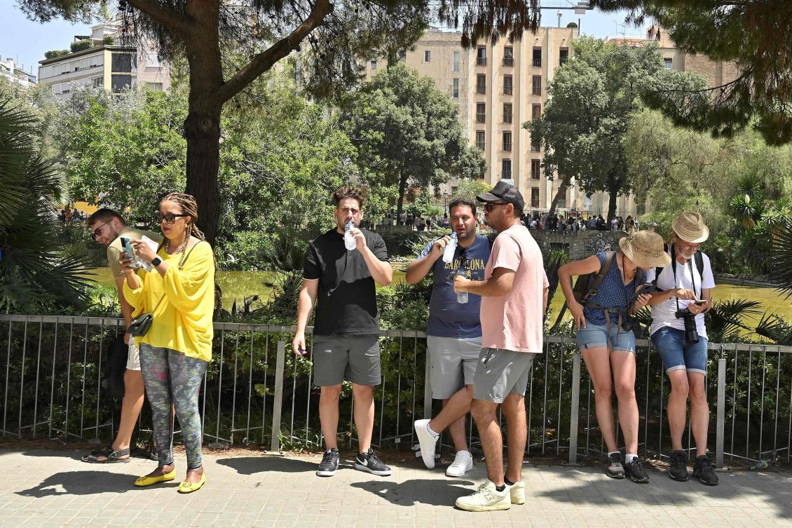 Tourists drink water as they stand in the shade of a tree near Sagrada Familia basilica in Barcelona on July 18, 2023. (AFP)